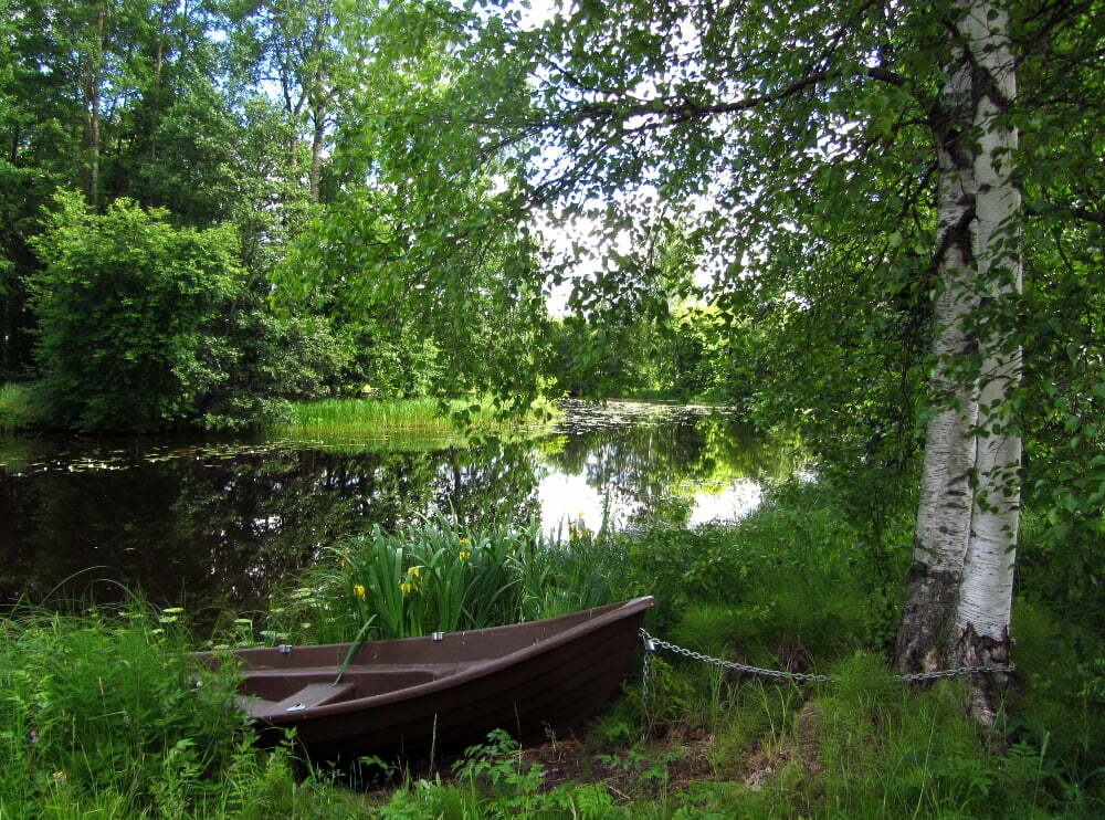 vanha vene joen rannassa kesäisen vehreässä maisemassa