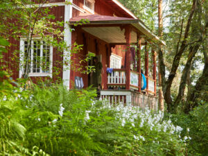 Punainen huvila, jossa on valkoisia koristeellisia yksityiskohtia. Kuistin edustalla on vihreitä lehtiä.