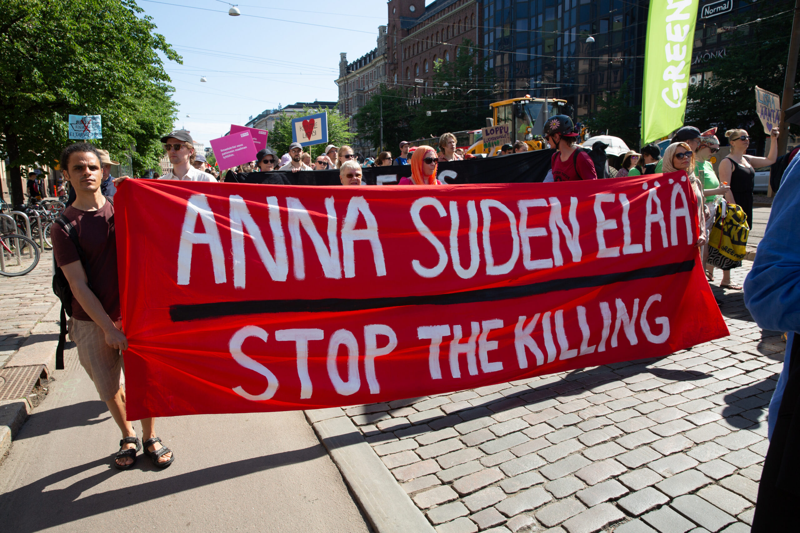 Mielenosoittajat marssivat kantaen punaista banderollia, jossa lukee: 